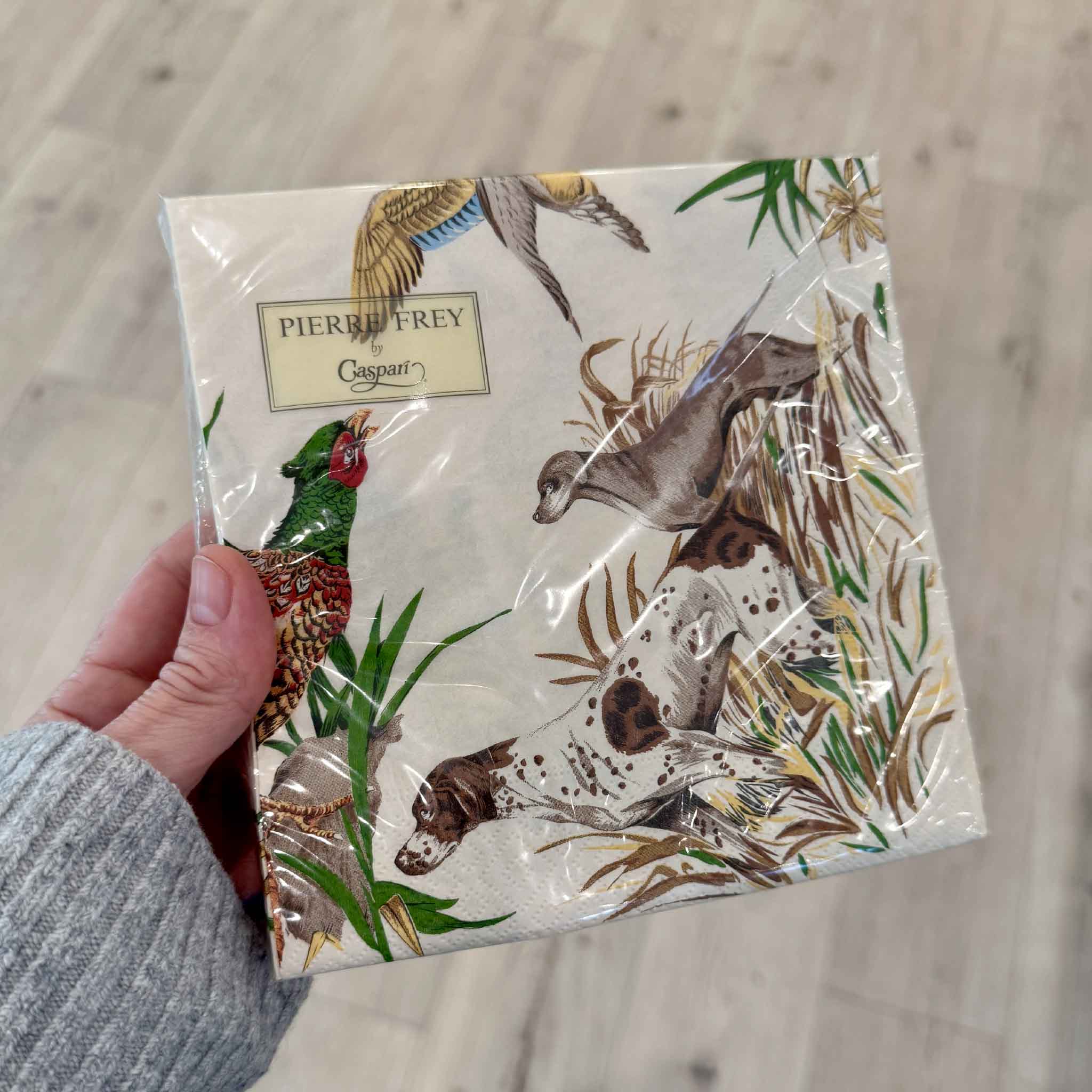 A package of Pierre Frey Sologne luncheon napkins by Caspari held inside Gray Man Gallery in Pawleys Island, South Carolina. The detailed sporting design showcases hunting dogs, a pheasant, and woodland scenery inspired by the French countryside. Printed in Germany on FSC-certified triple-ply paper with non-toxic, food-safe inks, these premium napkins are ideal for sporting enthusiasts, bird hunters, dog lovers, fall entertaining, and elegant hostess gifts.