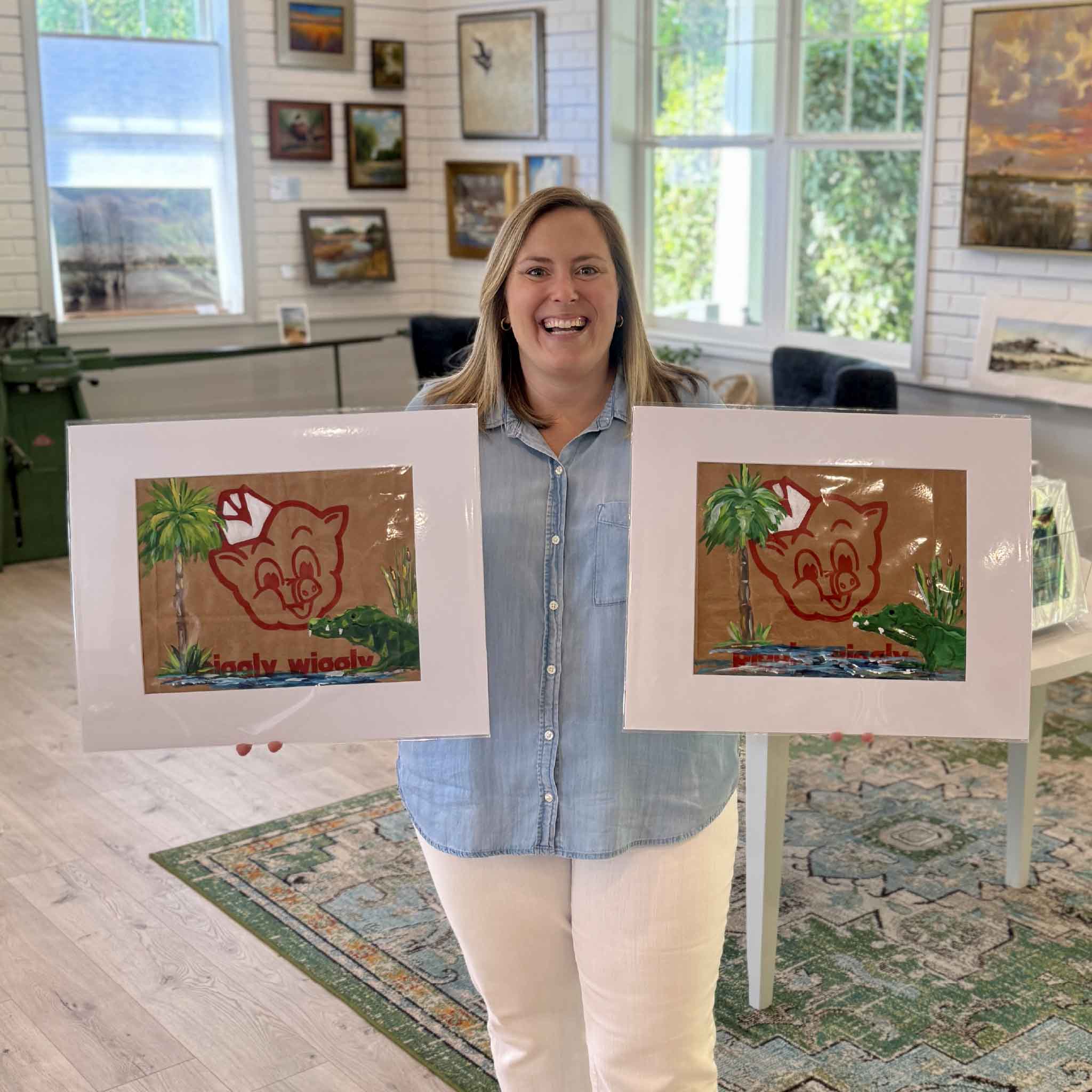 Gray Man Gallery team member holding two Piggly Wiggly Palmetto Gator paintings by local artist Jenny Reynolds, showing variation and scale of artwork painted on authentic grocery bags