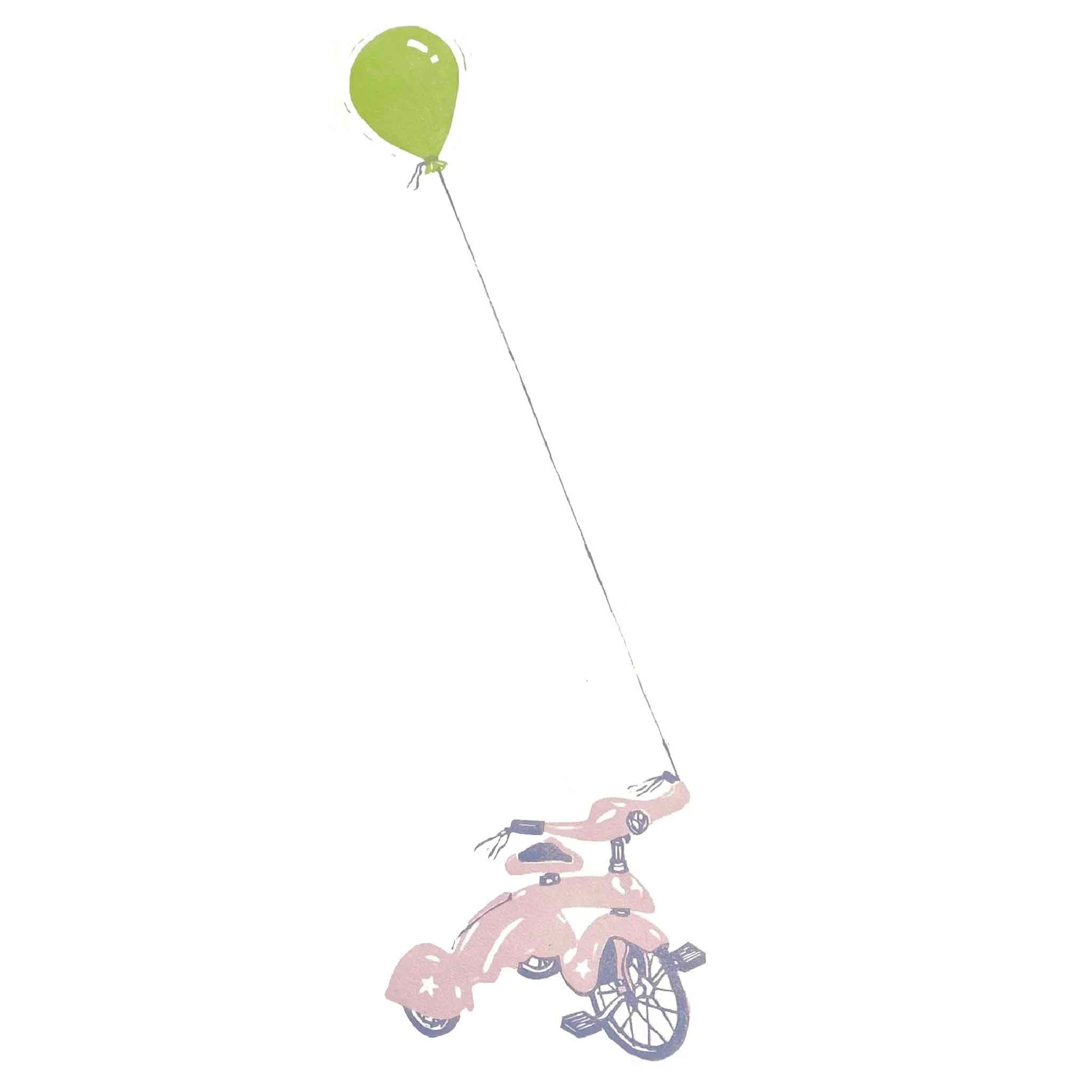 Detail view of Pink Wheels, an original linocut by local artist Laurie McIntosh, showing a pink tricycle tethered to a green balloon, printed on cotton paper and framed at Gray Man Gallery in Pawleys Island, South Carolina.