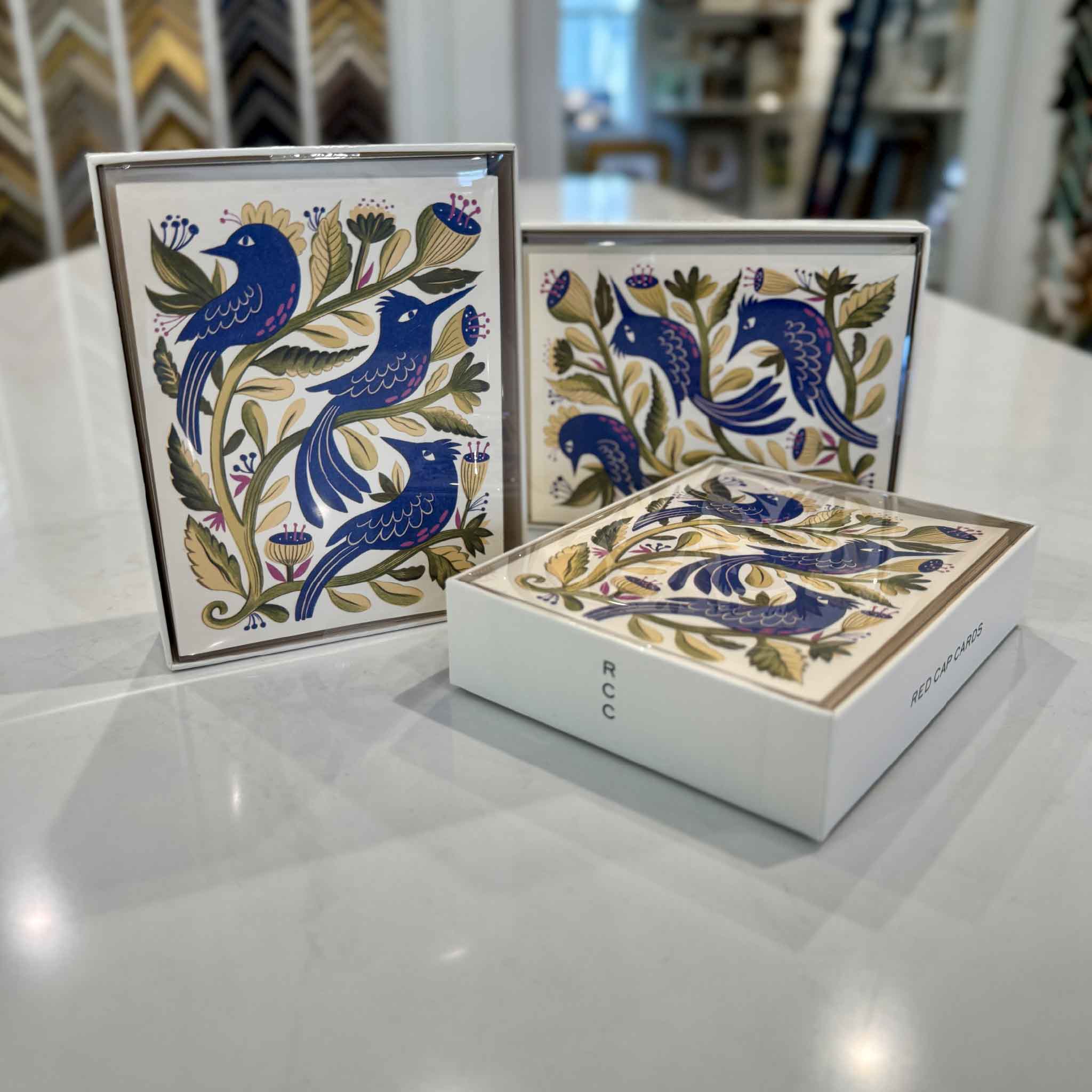 Boxed set of eight Purple Birds notecards by Melissa Castrillon displayed inside Gray Man Gallery in Pawleys Island, with matching botanical bird cards and presentation box shown together.