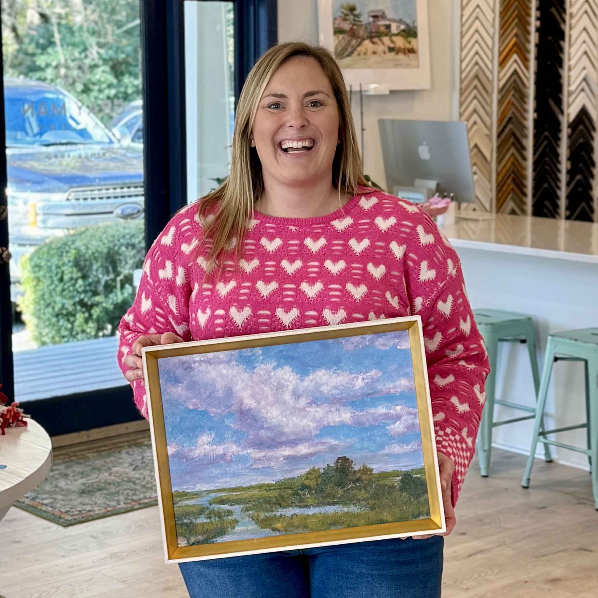 Bordy holding Purple Majesty, an original oil painting from Jeanne O’Neal’s Divine Connection series, featuring a Lowcountry marsh and lavender sky, 12x16 framed in gold at Gray Man Gallery in Pawleys Island, South Carolina