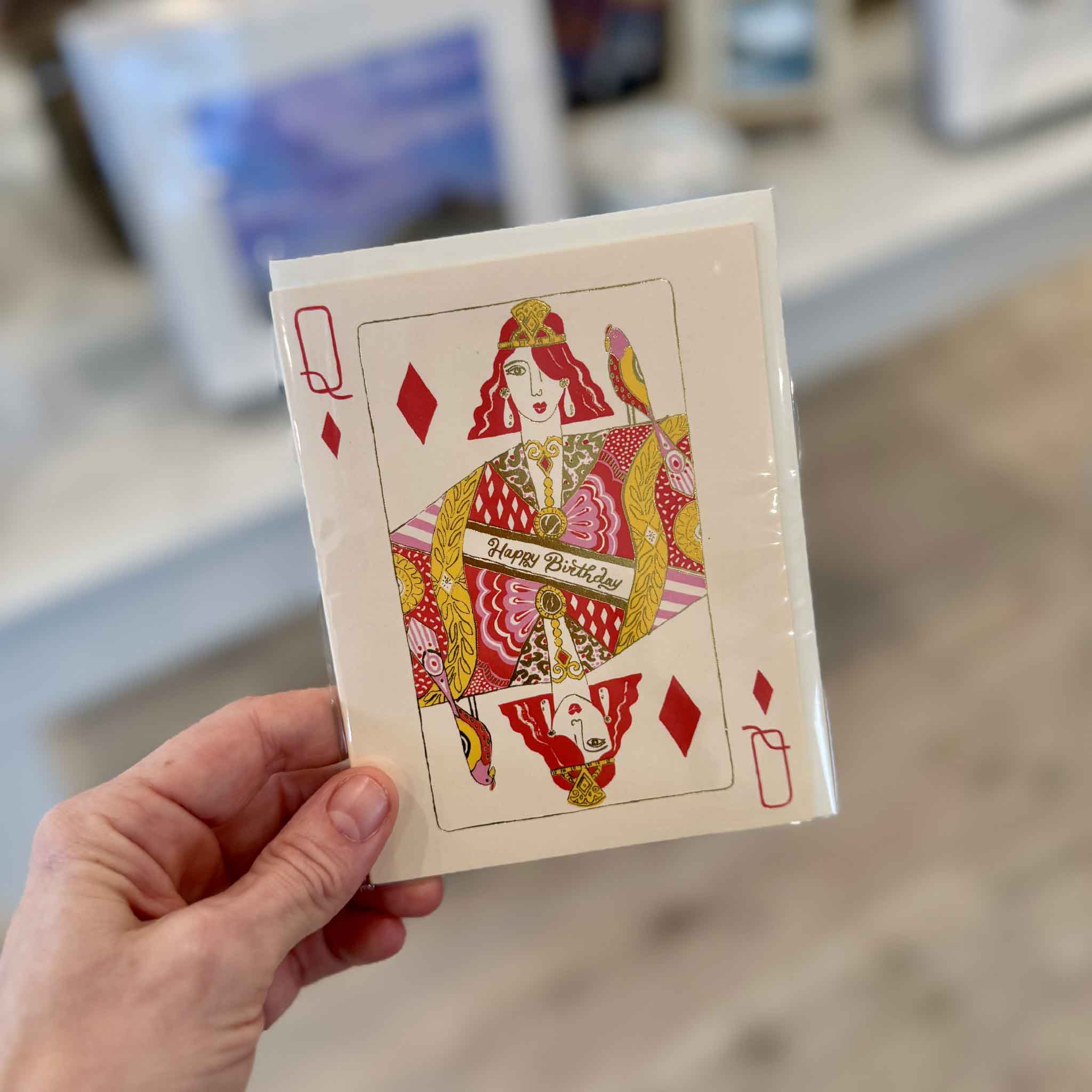 Hand holding the Queen of Diamonds birthday card, a playful birthday card for women featuring a hot pink playing card queen with metallic gold foil details and a “Happy Birthday” sash, available at Gray Man Gallery in Pawleys Island, South Carolina.