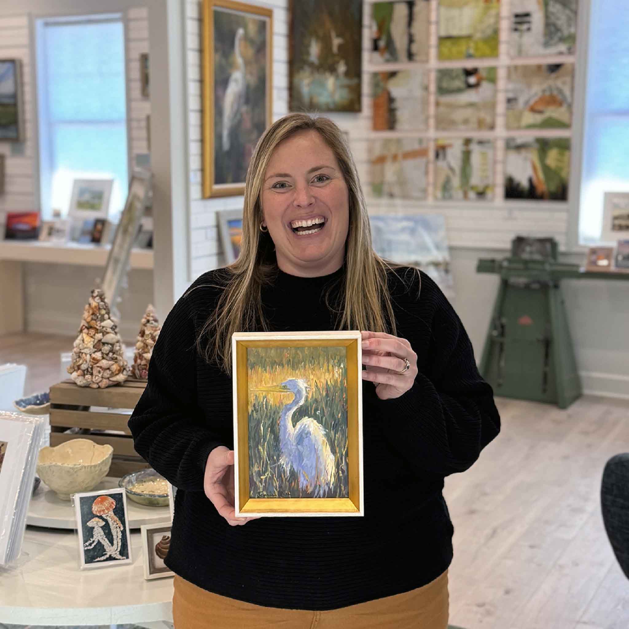 Local artist Jeanne O’Neal original oil painting “Quietly Watching” 6x9 featuring a white egret in Lowcountry marsh, shown at Gray Man Gallery in Pawleys Island, South Carolina with gallery team member Bordy