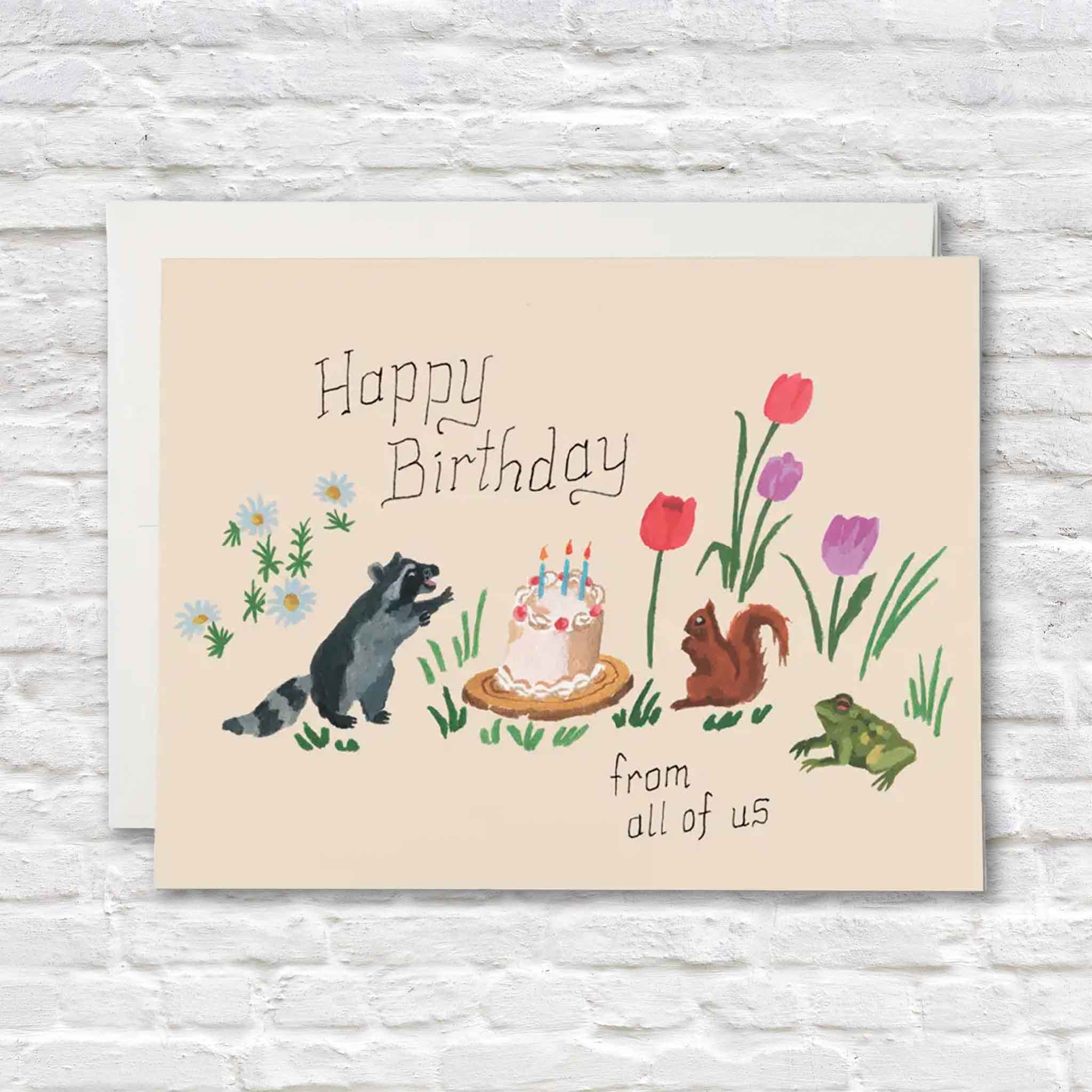 Red Cap Cards "Birthday Critters" greeting card illustrated by Danielle Kroll displayed with its matching envelope inside Gray Man Gallery in Pawleys Island, South Carolina. The cheerful birthday card features woodland animals gathered around a birthday cake surrounded by colorful spring flowers.