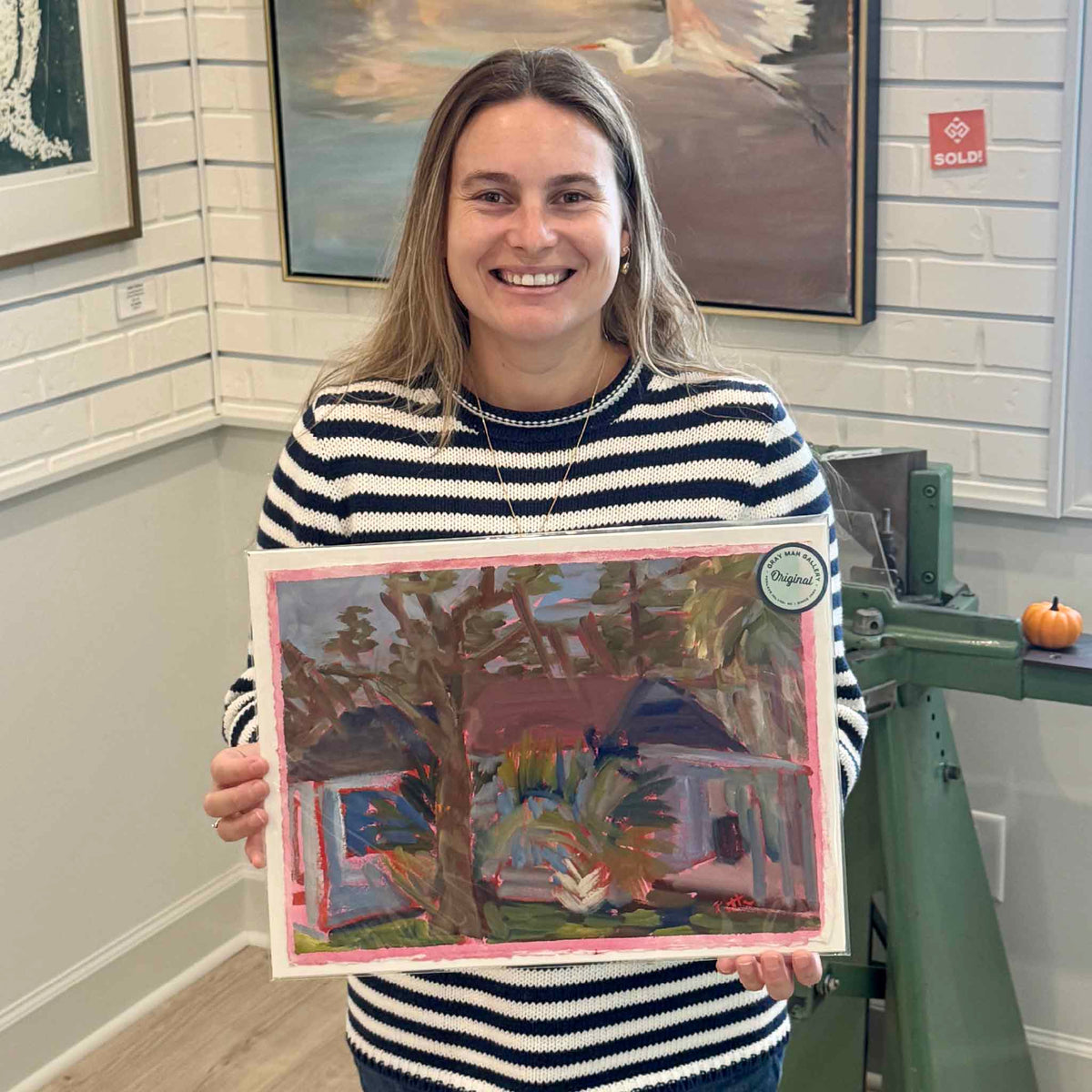 Gray Man Gallery team member holding Jamie’s House #214, an original oil on paper by local artist Retta Dotterer, showing the scale, expressive wooded landscape and signature pink painted border.