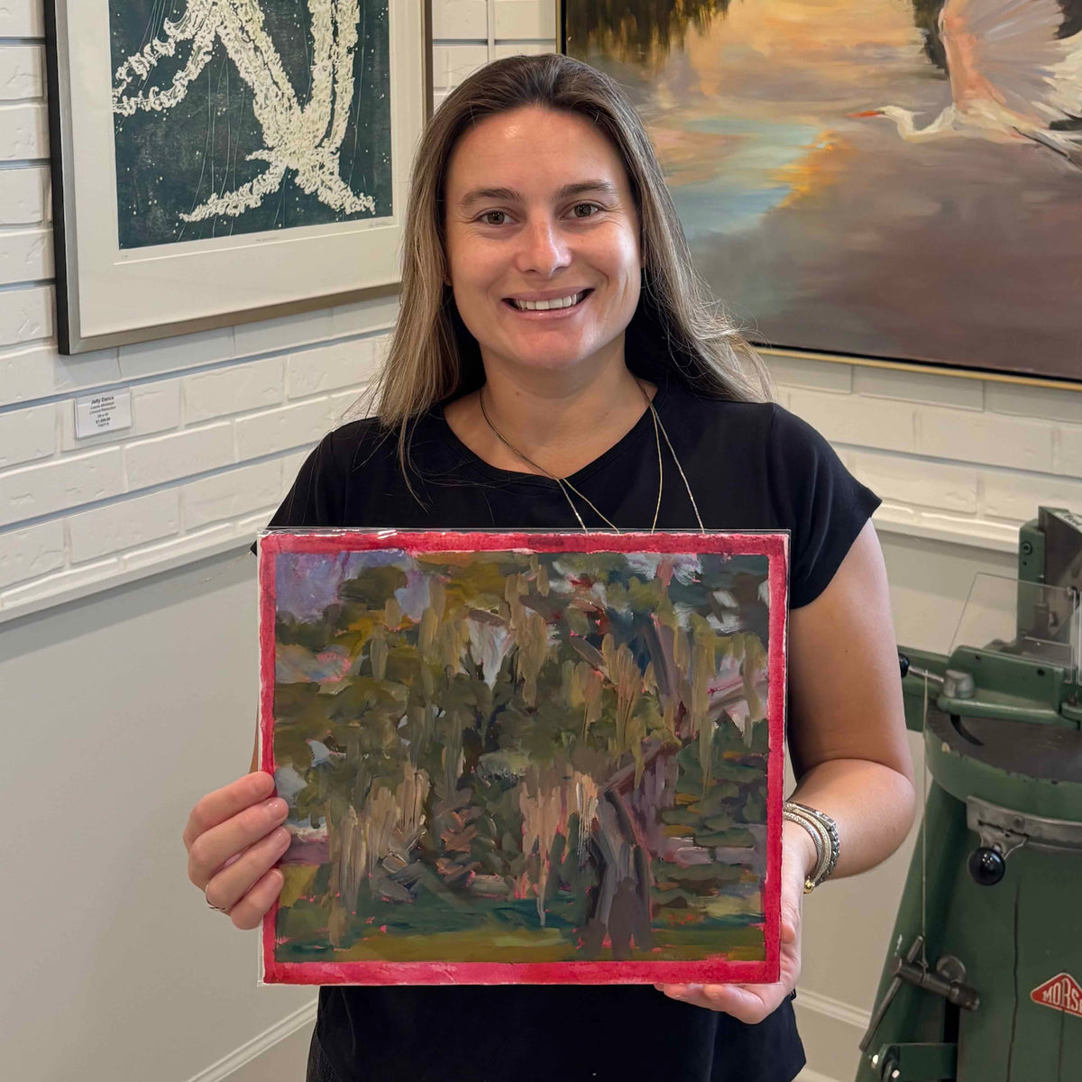 Gray Man Gallery team member holding Magnolia Cemetery I #218, an original oil on paper by local artist Retta Dotterer inspired by Charleston’s Magnolia Cemetery, showing the scale, moss-draped landscape, and signature pink border.