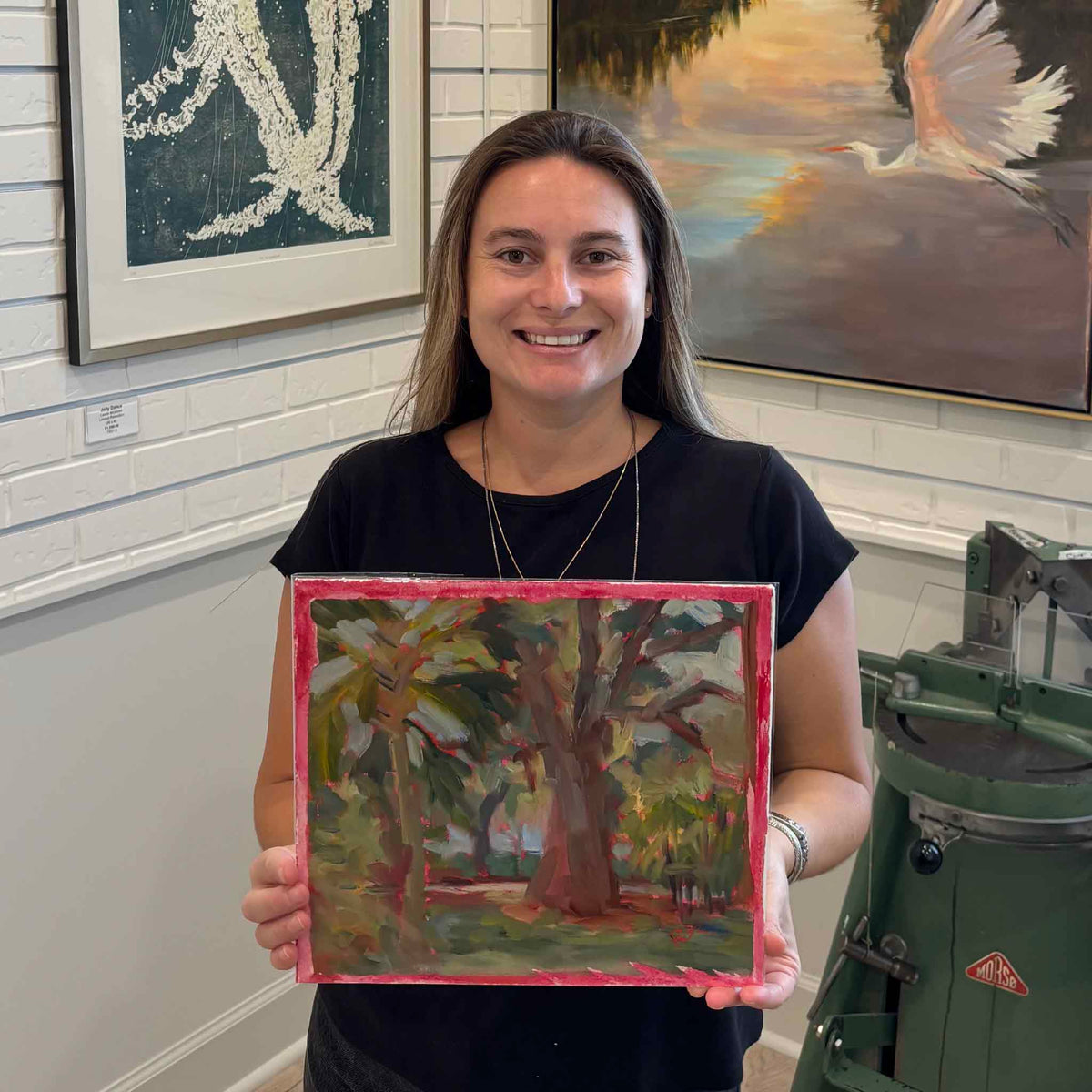 Gray Man Gallery team member holding Palmetto and Oak #221, an original oil painting by local artist Retta Dotterer featuring a Lowcountry live oak and palmetto in expressive green and earthy tones, shown for scale at Gray Man Gallery in Pawleys Island, South Carolina.