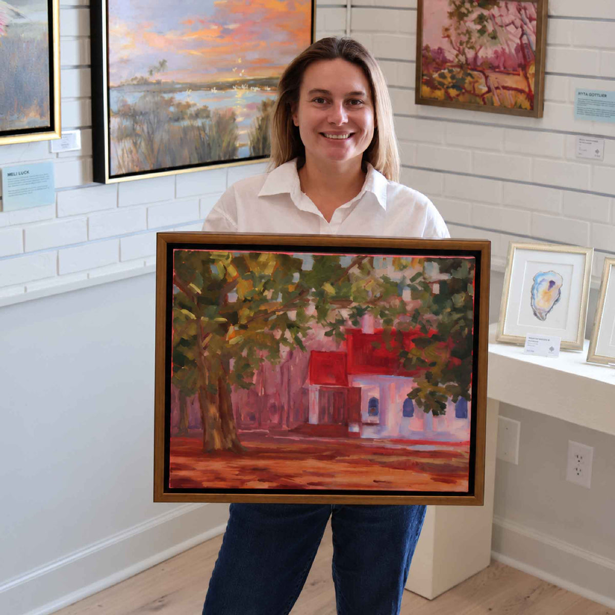 Gray Man Gallery team member holding South Santee Church #160, an original oil painting by local artist Retta Dotterer featuring a white Lowcountry church with a red roof beneath leafy trees, shown for scale at Gray Man Gallery in Pawleys Island, South Carolina.