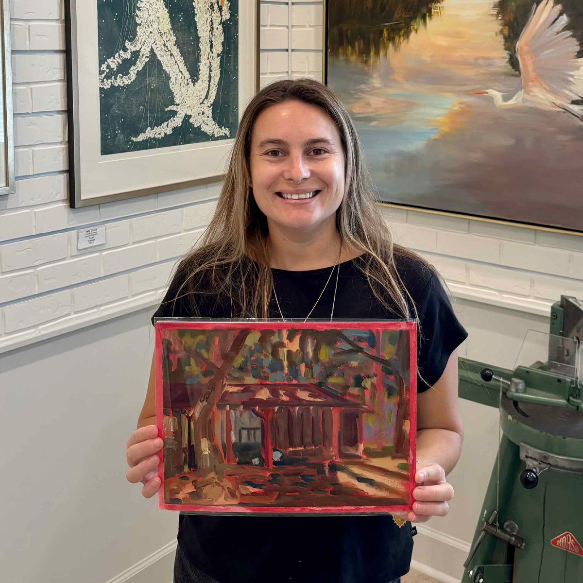 Gray Man Gallery team member holding Yawkey Shed #205, an original oil on paper by local artist Retta Dotterer, showing the scale and vivid hand-painted border inside the Pawleys Island gallery.