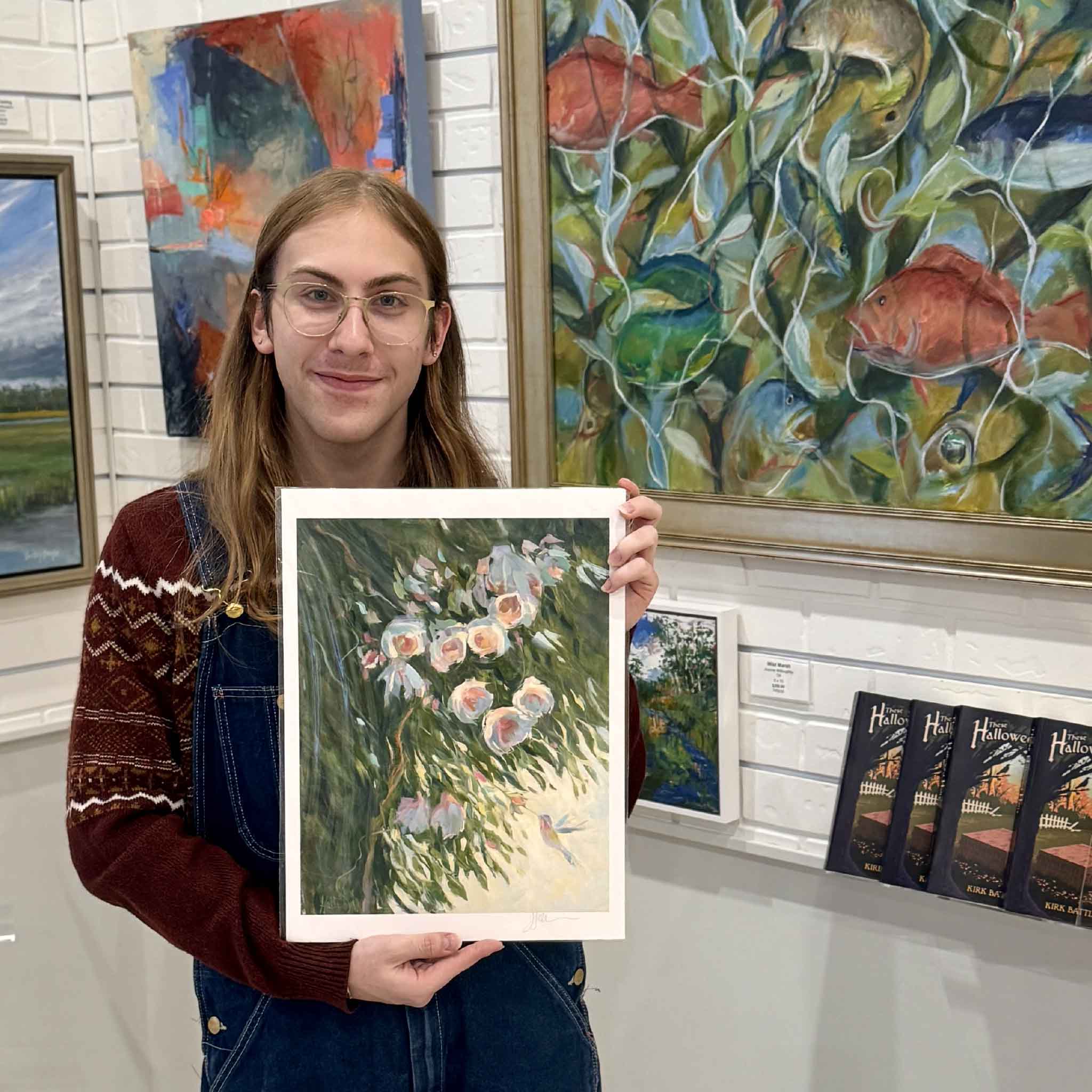 A Gray Man Gallery team member holds the Seeking Nectar print by Helli Luck, showing the delicate camellias and hummingbird design in a standard frame-ready size.