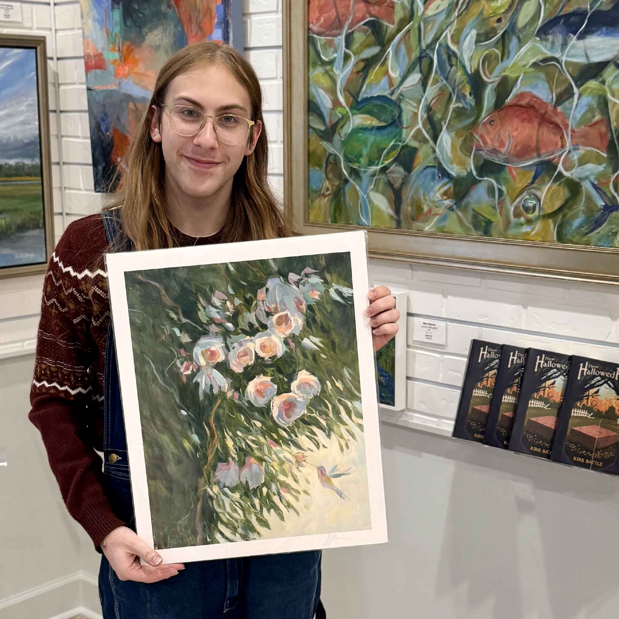A Gray Man Gallery team member holds the Seeking Nectar print by Helli Luck, showing the delicate camellias and hummingbird design in a 16x20 standard frame-ready size.