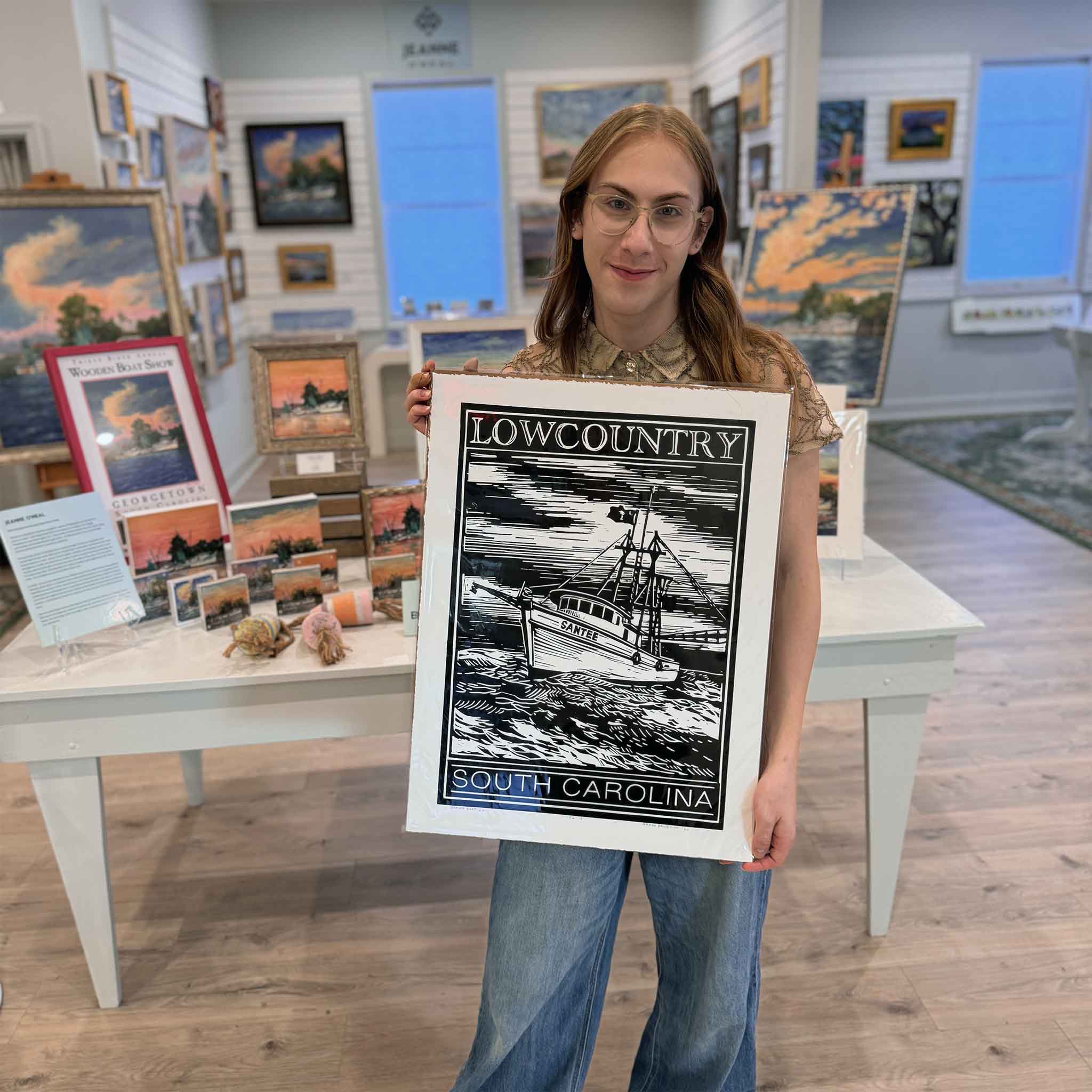 Alex holding the Shrimp Boat linocut print in black by Aaron Baldwin inside Gray Man Gallery.