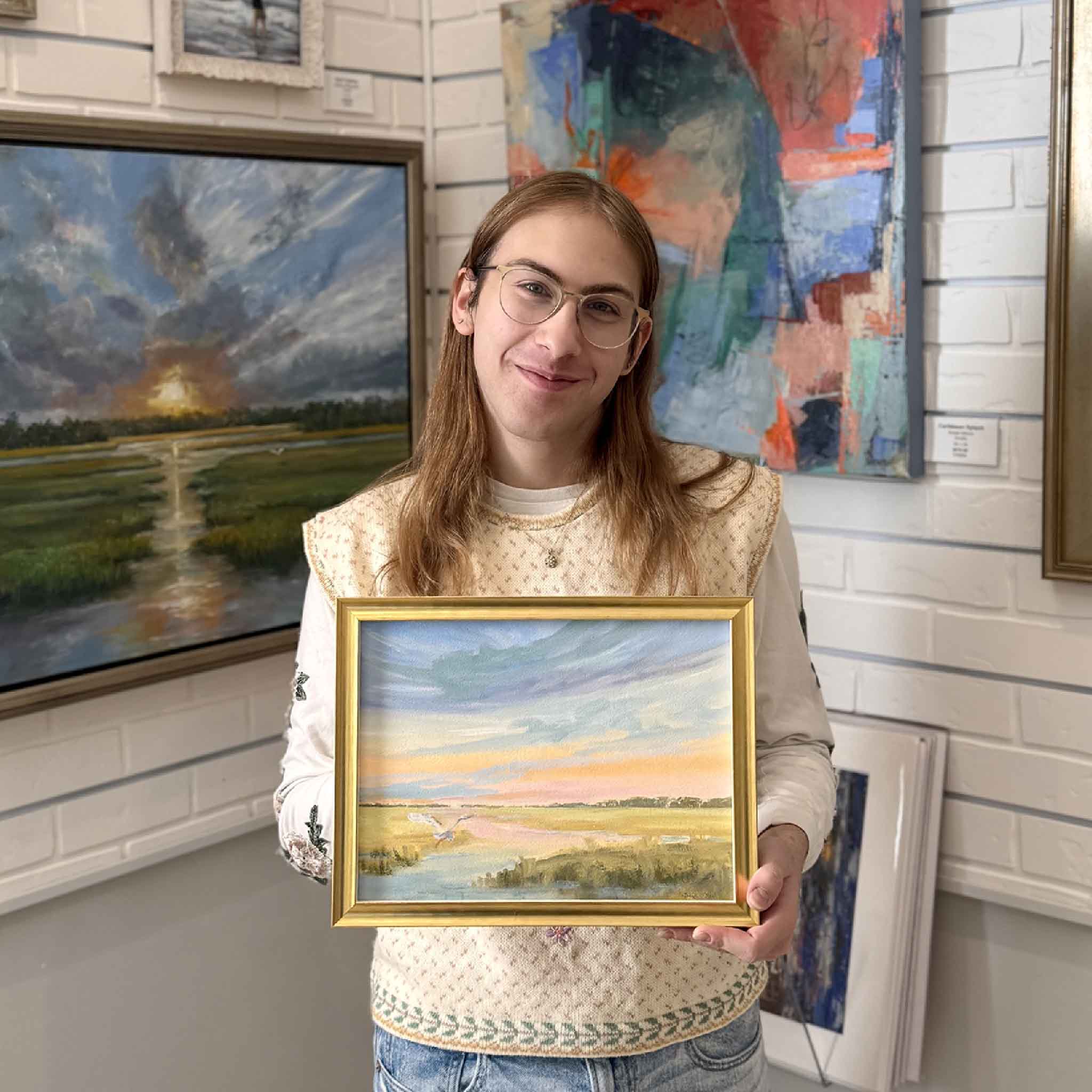 Gallery assistant holding Slice of Heaven by Jeanne O’Neal, a framed coastal marsh oil painting in a gold frame.