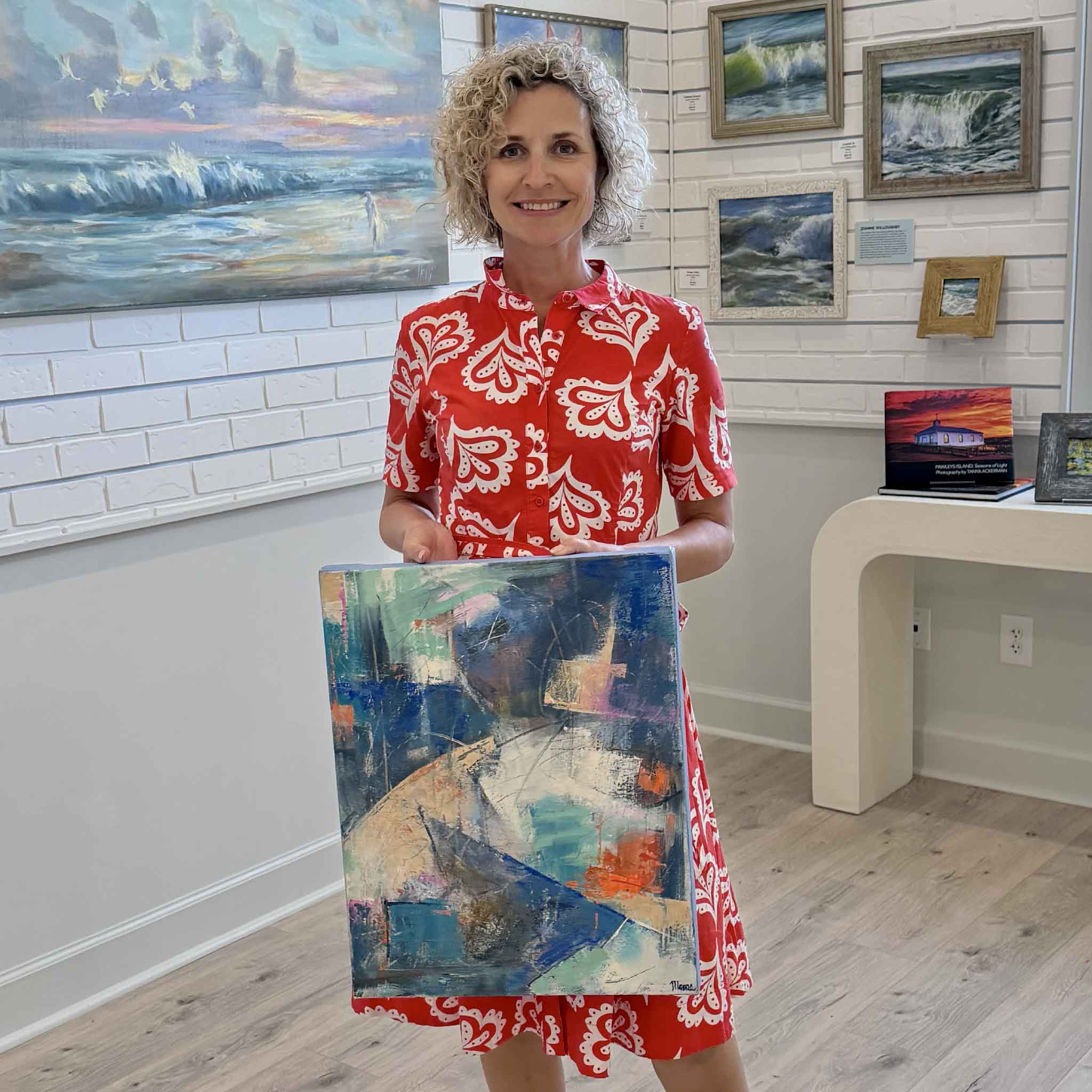 Local artist Susan Moore holding her original abstract acrylic painting Summer Solstice inside Gray Man Gallery Pawleys Island showing scale of the gallery wrapped canvas with layered color and expressive movement
