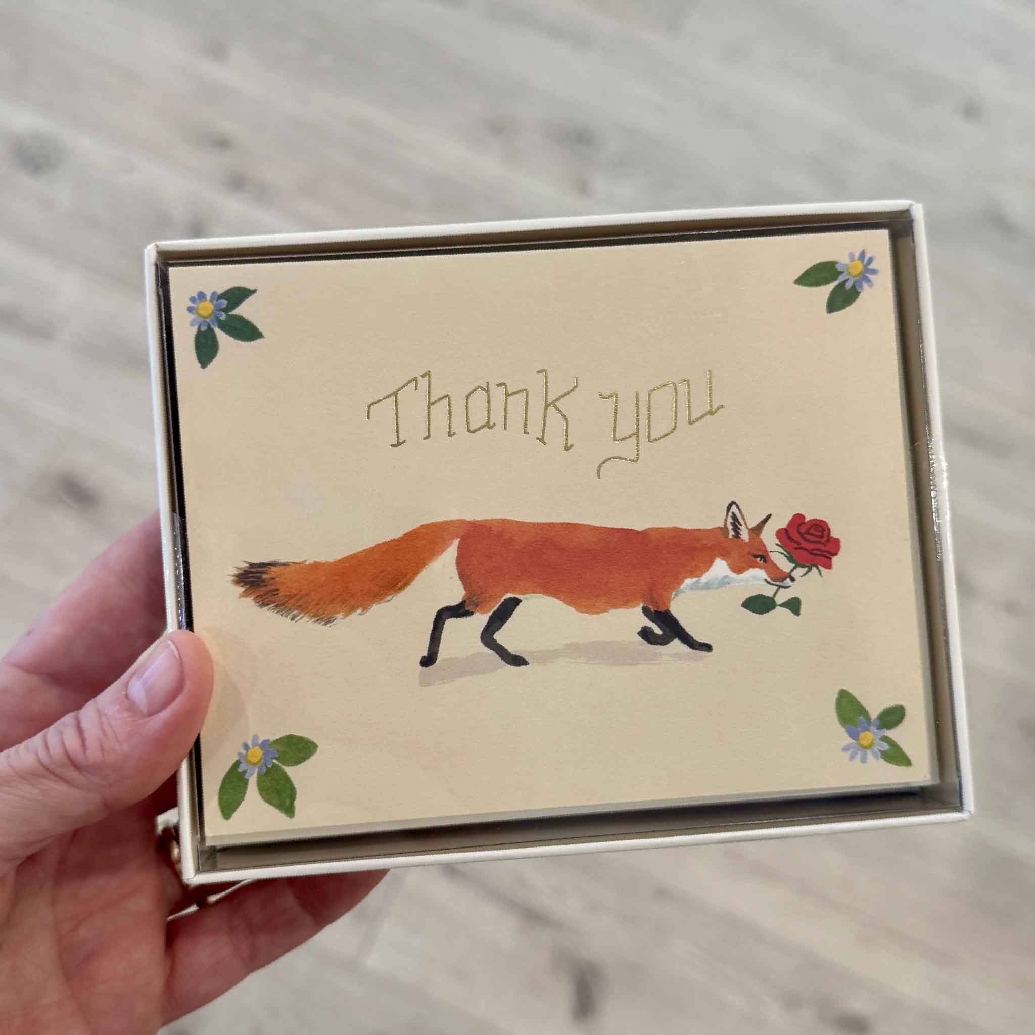 Boxed set of Thank You Fox greeting cards by Danielle Kroll displayed in gift packaging at Gray Man Gallery in Pawleys Island, South Carolina. Each card features a graceful fox carrying a red rose beneath gold foil "Thank You" lettering, making this elegant boxed stationery set perfect for keeping thoughtful thank-you cards on hand for every occasion.