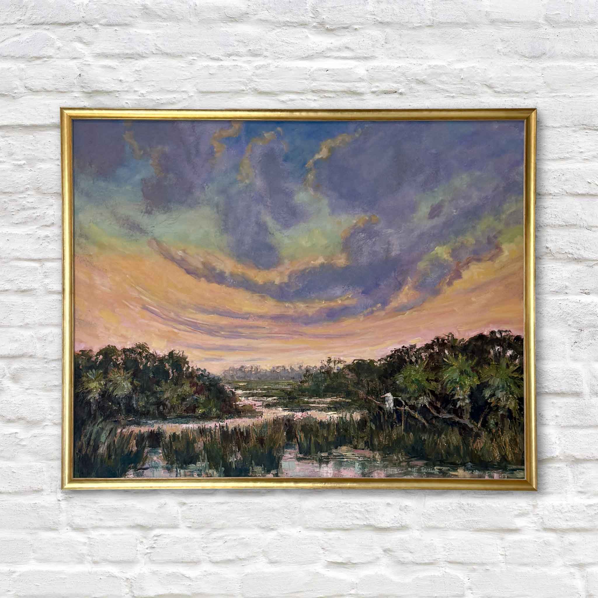 The Day Softens, an original oil painting by Jeanne O'Neal, framed in her signature gold frame and available at Gray Man Gallery in Pawleys Island. A dramatic Lowcountry sunset fills the sky with sweeping lavender, blue, peach, and gold clouds above a winding tidal marsh and reflective coastal water.