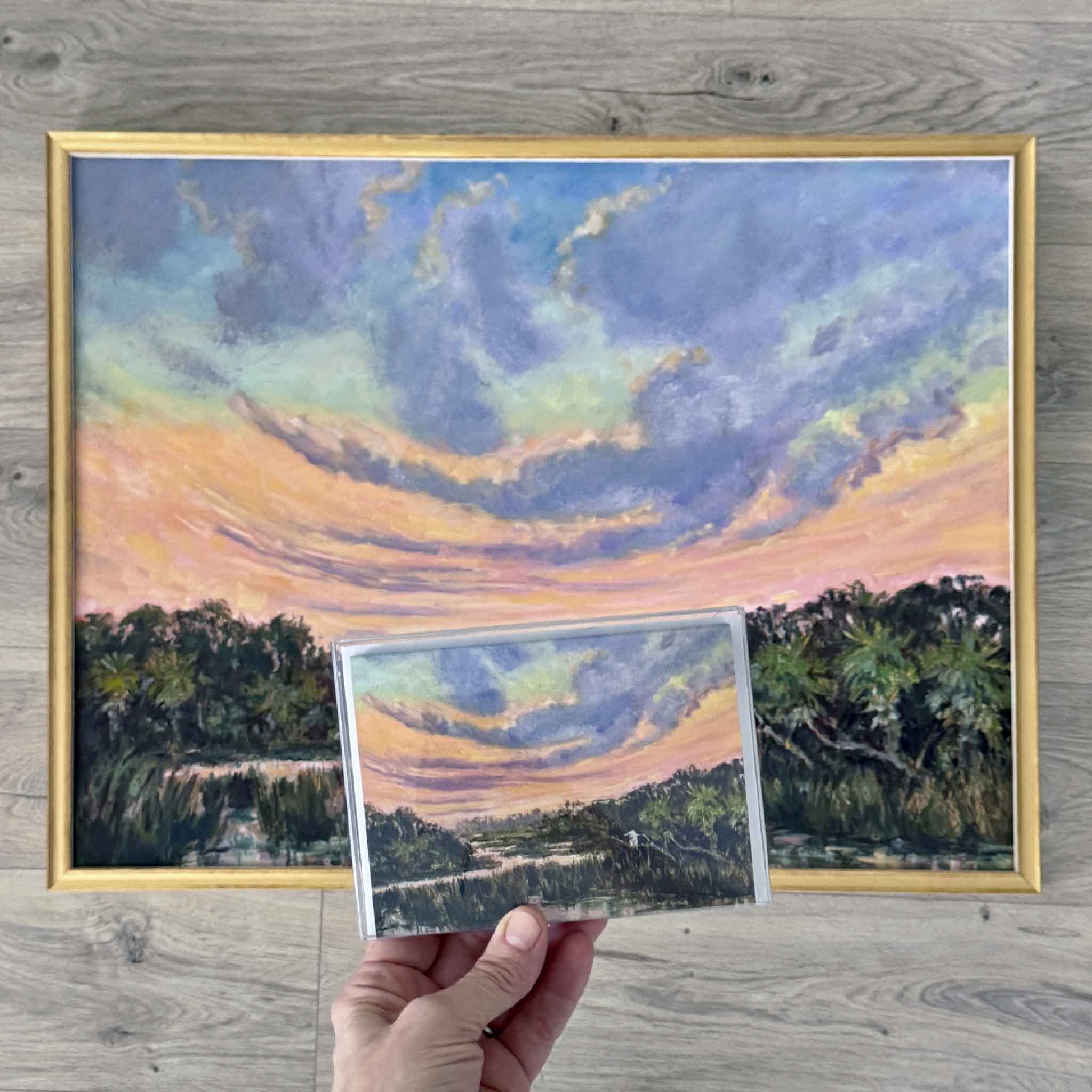 Jeanne O'Neal's original oil painting The Day Softens displayed alongside the matching fine art notecard, highlighting the dramatic Lowcountry marsh sunset and swirling pastel sky available at Gray Man Gallery in Pawleys Island.