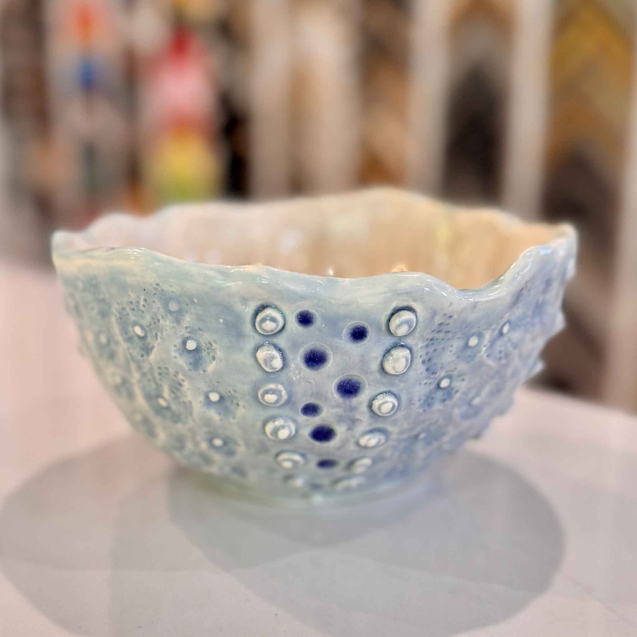 interior of Tidepool Texture Bowl by local artist Vida Miller featuring a glossy warm cream glaze with soft tonal variation and light reflection contrasting the raised barnacle-like texture and seafoam blue exterior at Gray Man Gallery Pawleys Island