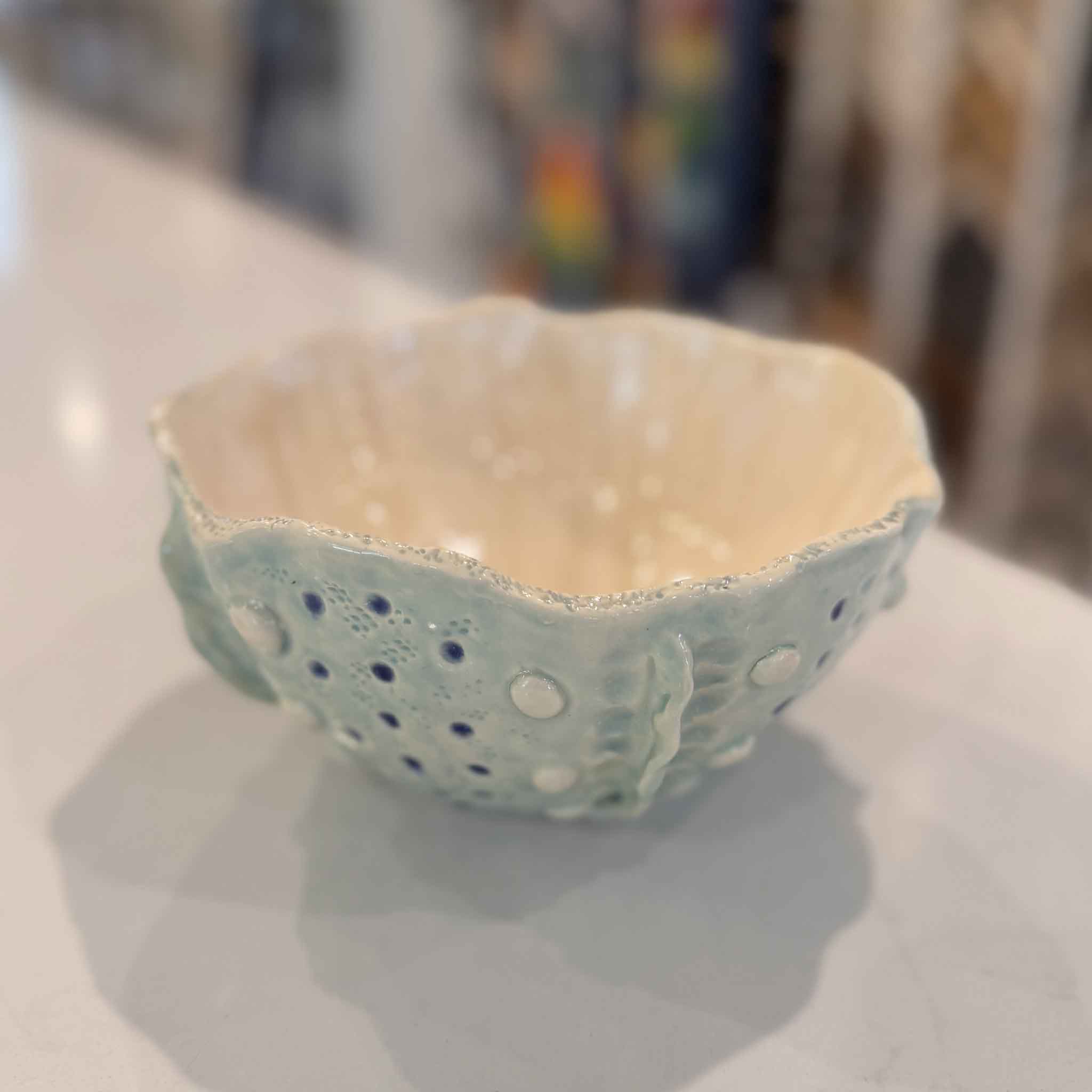 interior of Tidepool Texture Bowl by local artist Vida Miller featuring a glossy warm cream glaze with soft tonal variation and light reflection contrasting the raised barnacle-like texture and seafoam blue exterior at Gray Man Gallery Pawleys Island