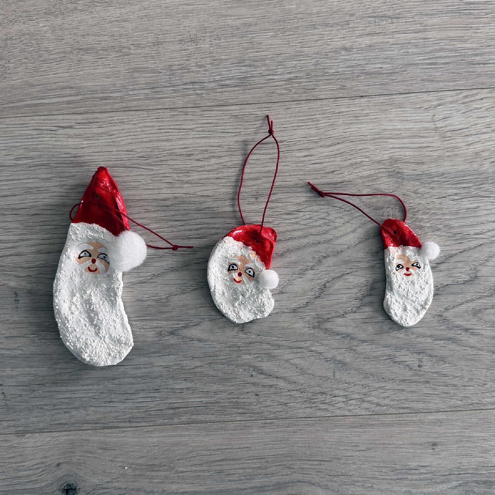 Hand-painted Santa oyster shell ornaments in small, medium, and large sizes by Tootsie Watkins displayed on a wooden surface