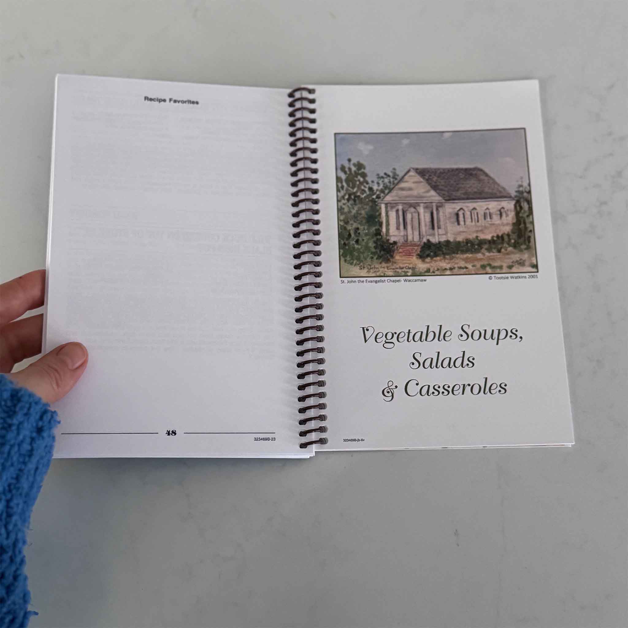 Interior pages of Tootsie’s Favorites: Pawleys Island Cookin’ cookbook by Tootsie Watkins, showing spiral binding, handwritten-style recipes, and original coastal artwork at Gray Man Gallery in Pawleys Island
