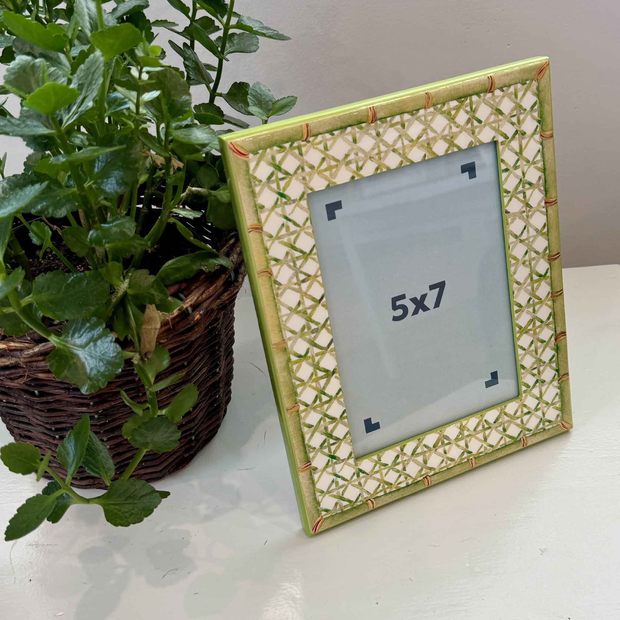 Trellis Green 5x7 lacquer picture frame styled beside a plant, showcasing its fresh coastal design and faux bamboo finish. Available at Gray Man Gallery, this decorative frame is ideal for displaying favorite photographs or small works of art in any home.