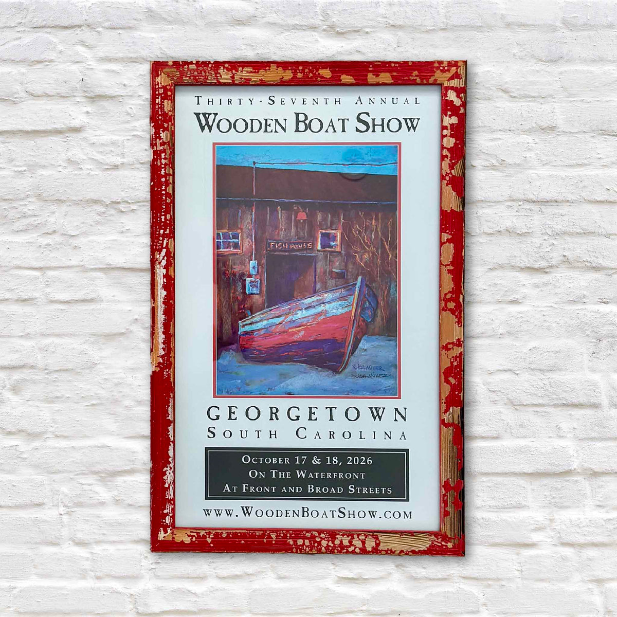 Official signed 2026 Georgetown Wooden Boat Show poster featuring Vida Miller's painting of the historic Georgetown Fish House and wooden boat, professionally presented in a distressed red frame at Gray Man Gallery in Pawleys Island, South Carolina.