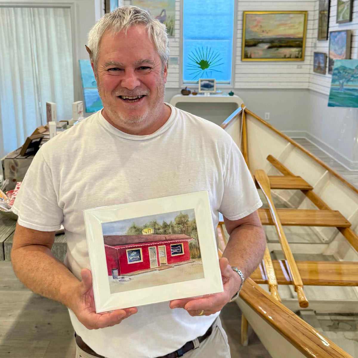 Lee, who personally visited the legendary Club 17 in Pawleys Island, South Carolina, smiling while holding an 8×10 watercolor art print of the historic red roadside establishment by local artist Vida Miller. Photographed inside Gray Man Gallery, celebrating an unforgettable piece of Lowcountry nightlife history.