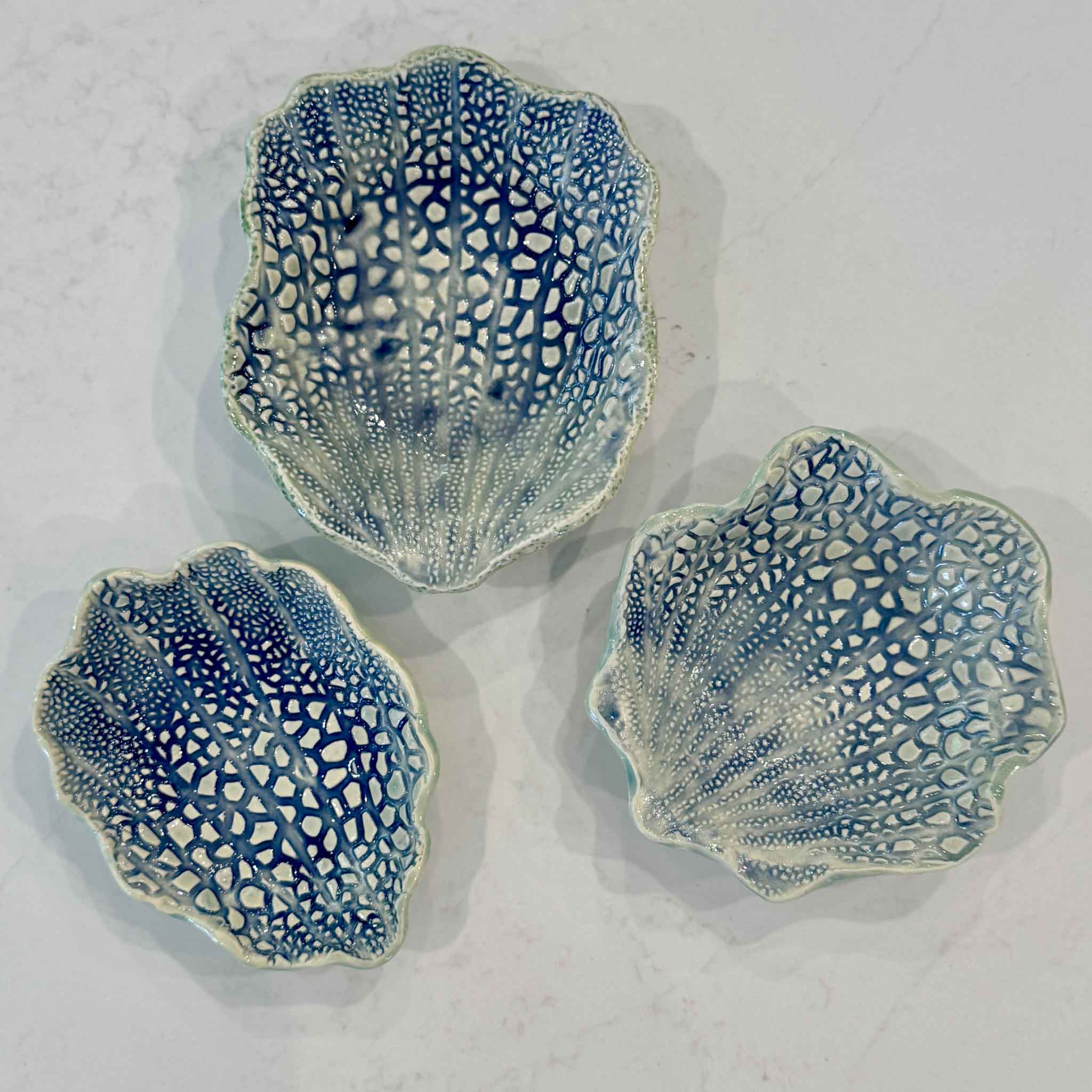 A collection of handmade Coral Shell Dishes by Vida Miller displayed together, highlighting the unique variations in shape, glaze, and handcrafted details that make every piece one of a kind. These South Carolina coastal pottery pieces are available at Gray Man Gallery in Pawleys Island.