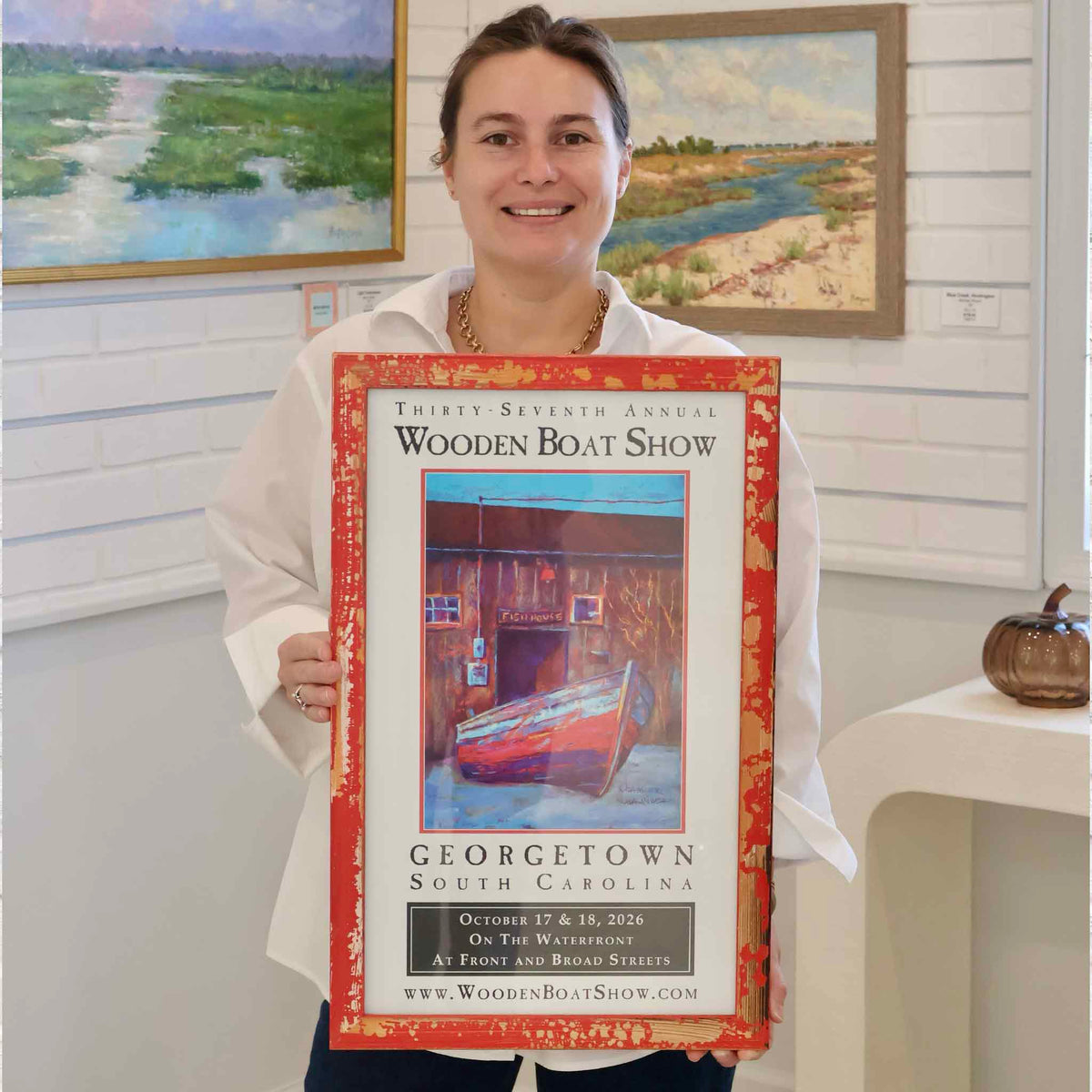 Framed and signed 2026 Georgetown Wooden Boat Show commemorative poster by local artist and Gray Man Gallery founder Vida Miller, shown in the Pawleys Island gallery to illustrate its finished size and distressed red frame.