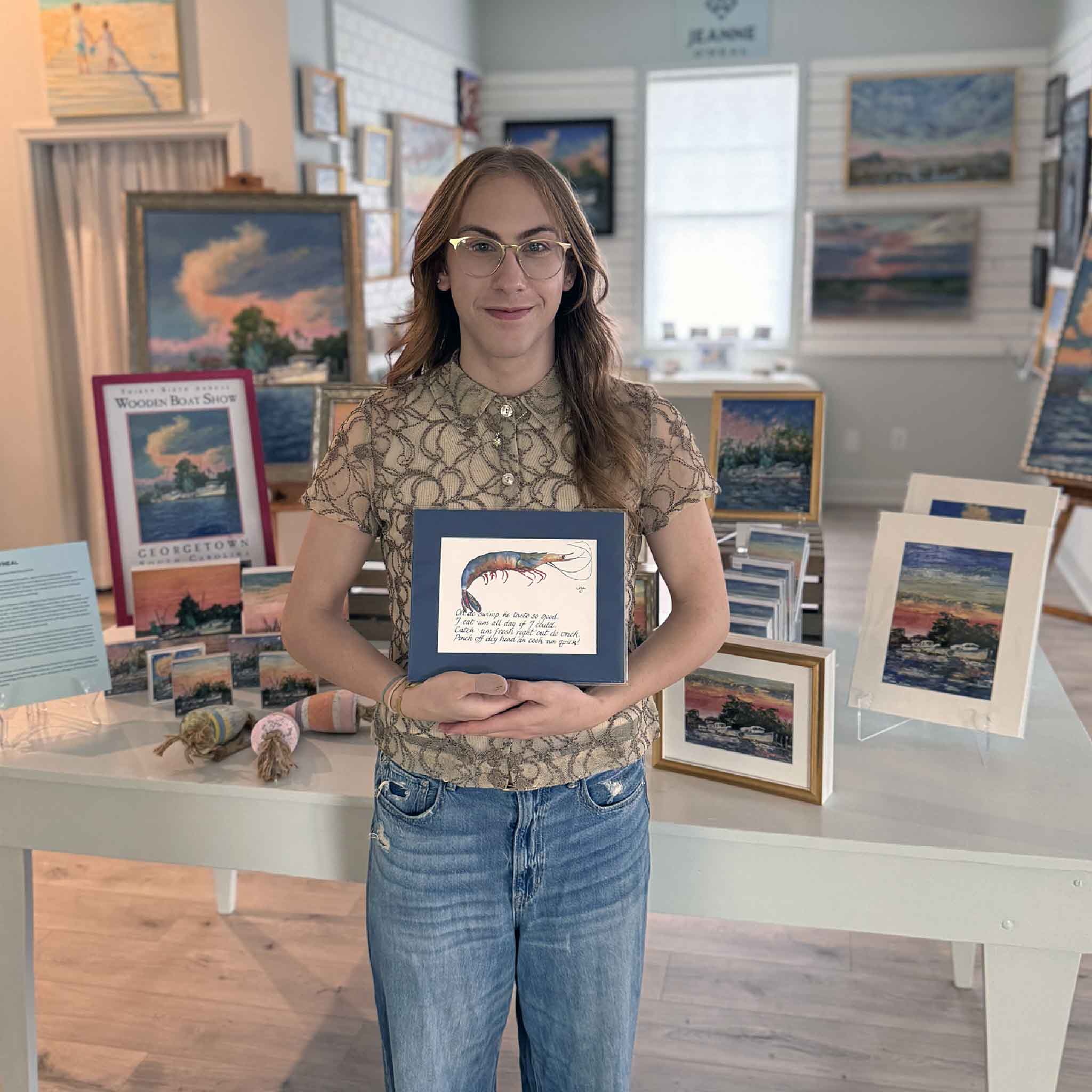 Alex holding “Gullah Odes: Shrimp” by local South Carolina artist Vida Miller inside Gray Man Gallery in Pawleys Island, featuring watercolor shrimp artwork with handwritten Gullah verse and Lowcountry coastal decor
