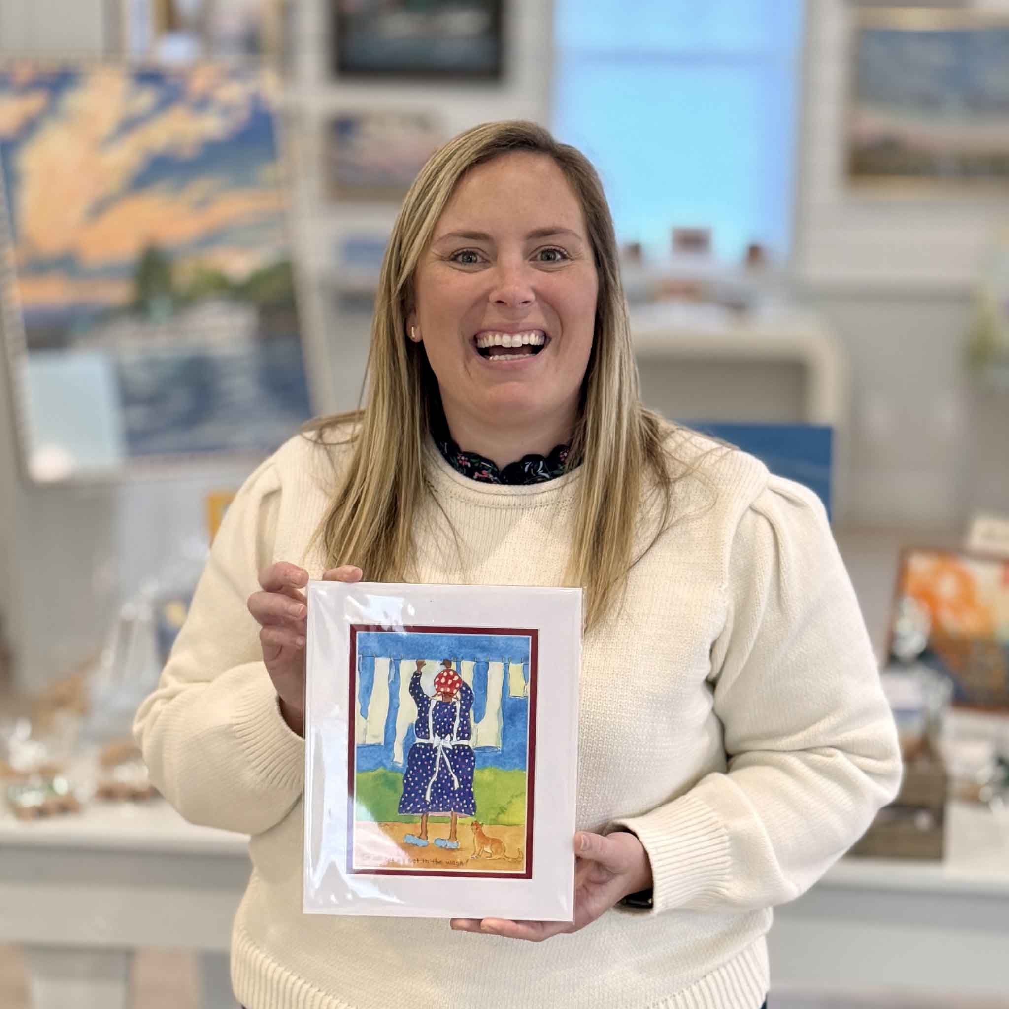 Local artist Vida Miller Little Ladies print titled It All Comes Out in the Wash, shown held in the Gray Man Gallery in Pawleys Island, South Carolina, featuring colorful laundry scene with playful Southern charm