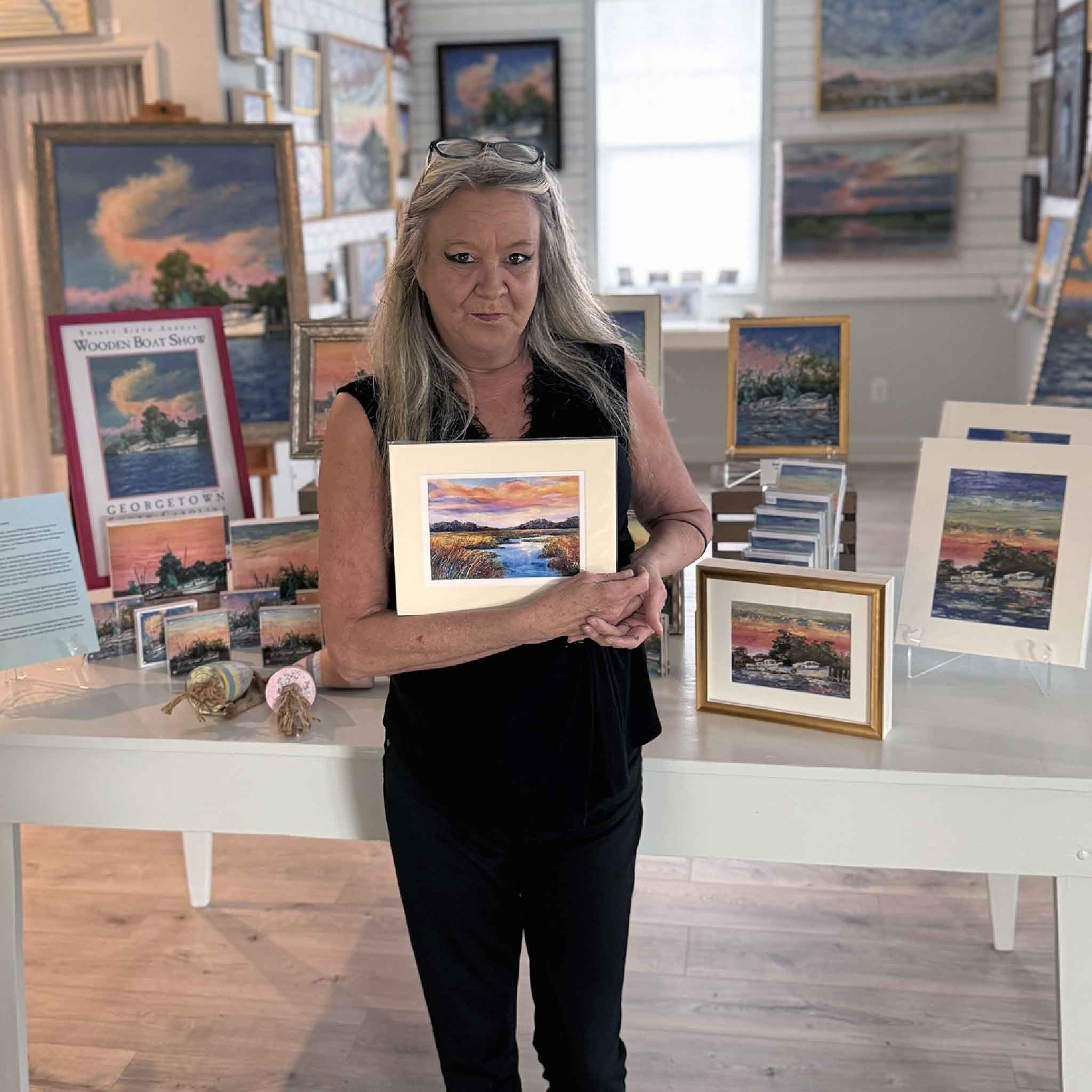 person holding Pawleys Island artist Vida Miller's professionally matted Marsh #5 pastel print inside Gray Man Gallery in Pawleys Island, South Carolina. This colorful Lowcountry marsh sunset reproduction showcases glowing evening skies, reflective tidal creeks, and rich coastal colors while providing an accurate sense of the artwork's display size.