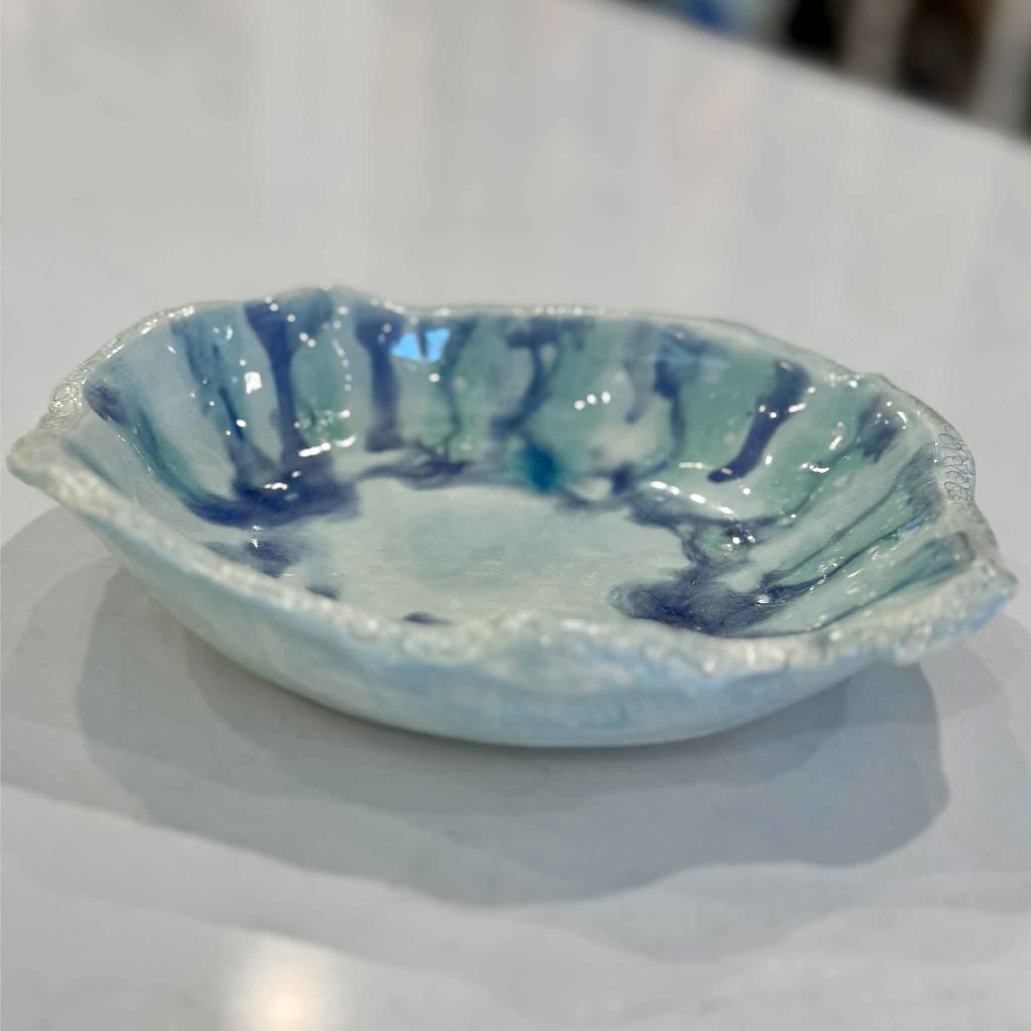 Handmade ceramic Marsh Drift Bowl by Vida Miller shown at an angle on a tabletop at Gray Man Gallery. The bowl features layered celadon, sea-glass blue, and deep indigo glaze movement inspired by Lowcountry tidal water and marsh landscapes.