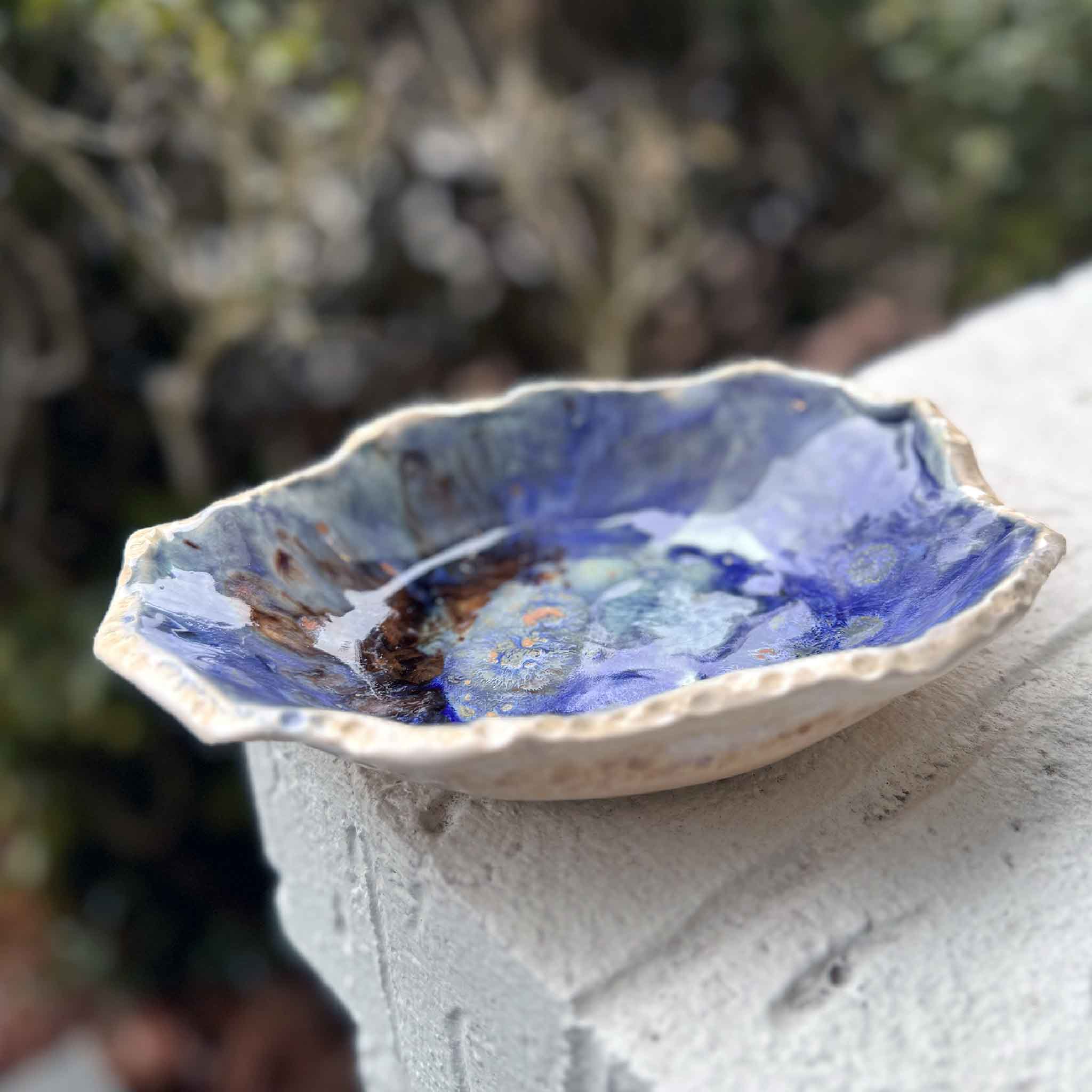 Medium deep blue handcrafted Lowcountry pottery bowl by Vida Miller, styled outdoors on a textured white ledge at Gray Man Gallery.